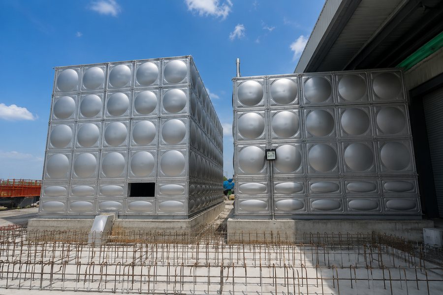 Two stainless steel water tanks on concrete plinths beside a plant building
